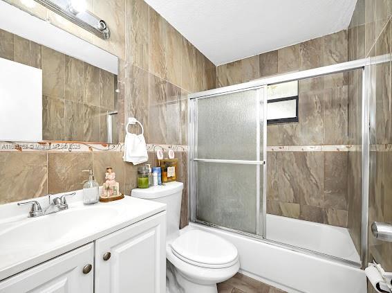 full bath with combined bath / shower with glass door, tile walls, toilet, and vanity