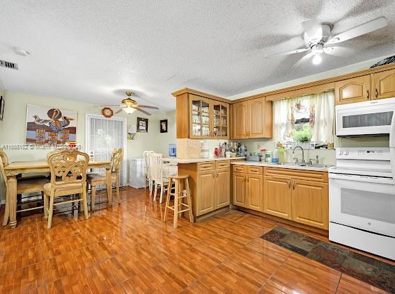 kitchen featuring glass insert cabinets, white appliances, light countertops, and a sink