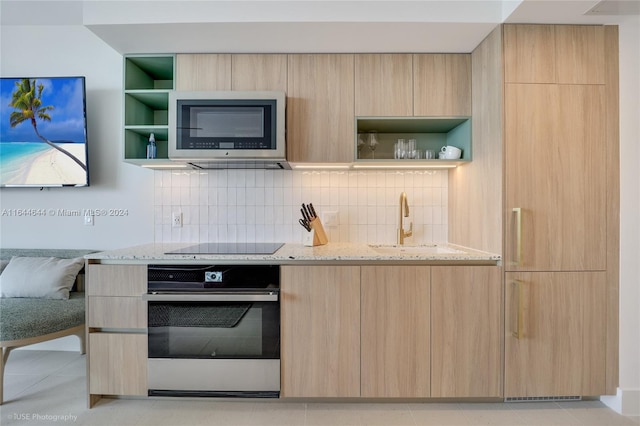 kitchen featuring black electric stovetop, light stone counters, oven, and light brown cabinets