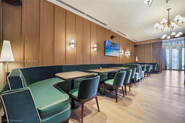 dining area featuring light wood-type flooring, wood walls, and a chandelier