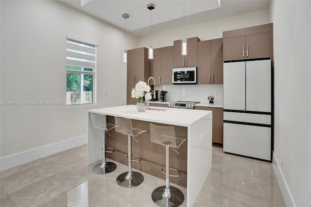 kitchen with pendant lighting, white refrigerator, an island with sink, stainless steel electric range, and a kitchen bar