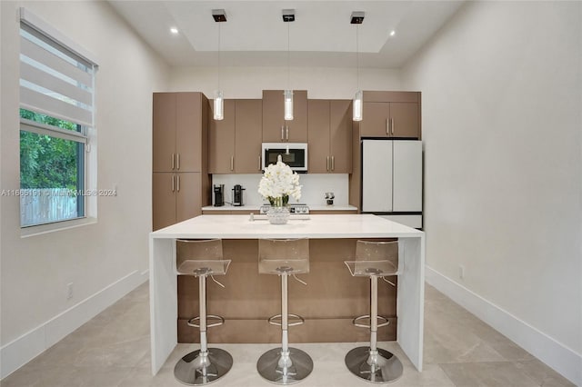 kitchen with a breakfast bar area, pendant lighting, white fridge, stainless steel range oven, and a center island with sink