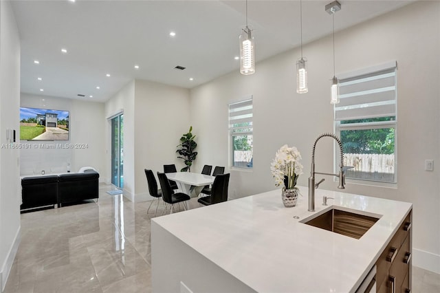 kitchen with a center island with sink, decorative light fixtures, sink, and a wealth of natural light