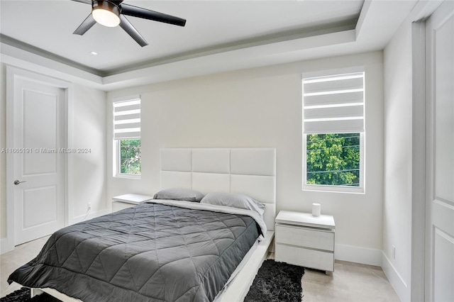 bedroom with ceiling fan, a tray ceiling, and multiple windows