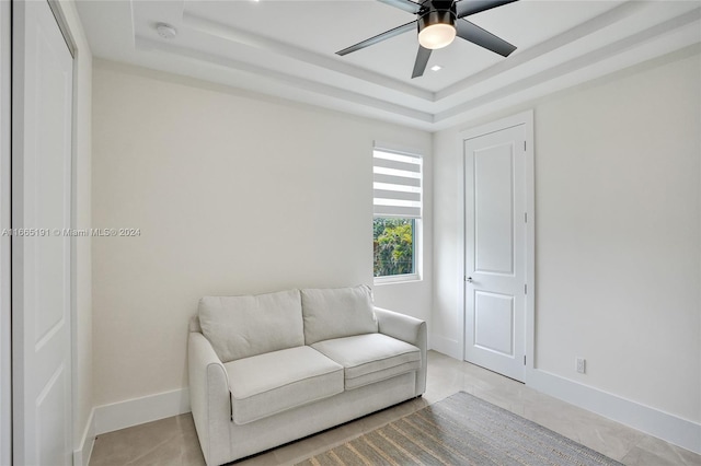 living area with a raised ceiling and ceiling fan