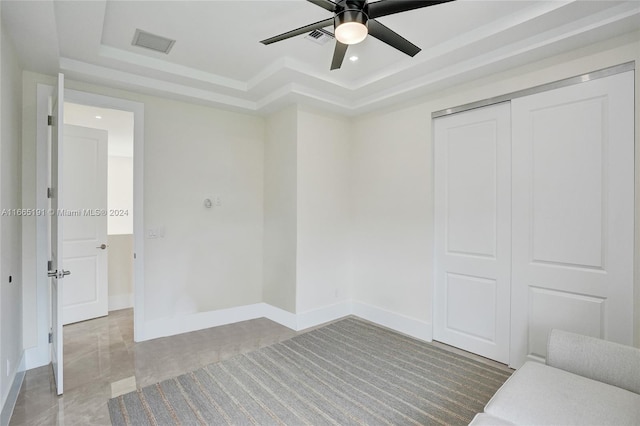 unfurnished bedroom with ceiling fan, a tray ceiling, and a closet