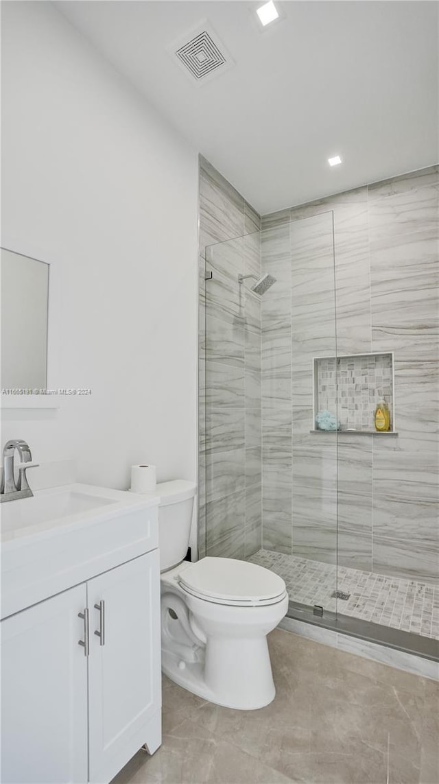 bathroom featuring a tile shower, tile patterned flooring, vanity, and toilet