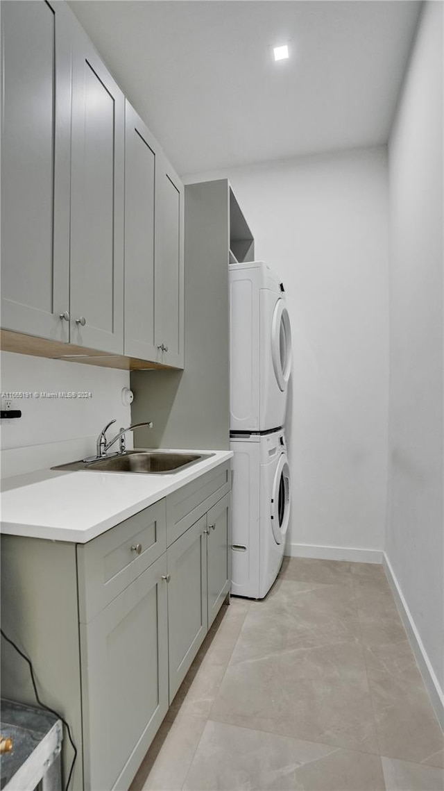 laundry room with cabinets, sink, and stacked washing maching and dryer