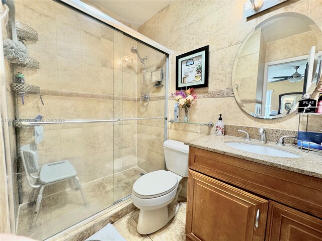 bathroom with vanity, a shower with shower door, tile walls, and toilet