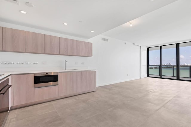 kitchen featuring sink, a water view, oven, light brown cabinetry, and expansive windows