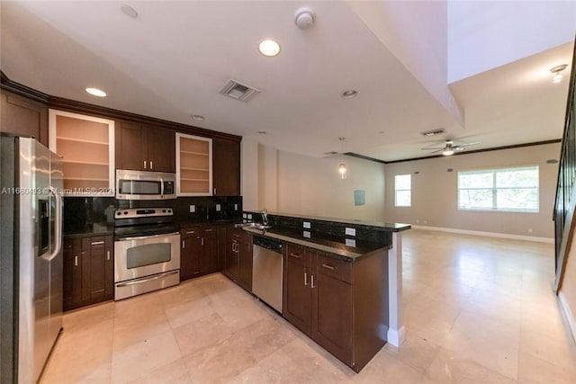 kitchen featuring dark brown cabinets, kitchen peninsula, stainless steel appliances, dark stone countertops, and ceiling fan