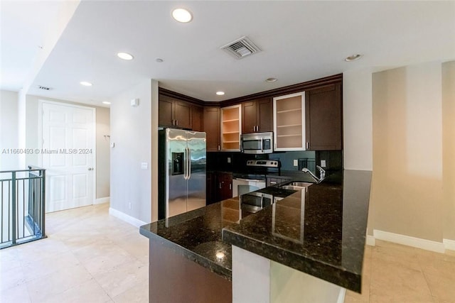 kitchen with kitchen peninsula, decorative backsplash, stainless steel appliances, dark brown cabinetry, and dark stone countertops