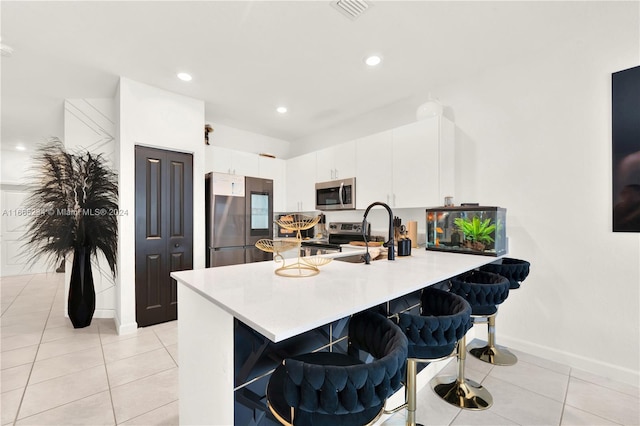 kitchen featuring light tile patterned flooring, a breakfast bar area, white cabinetry, kitchen peninsula, and stainless steel appliances