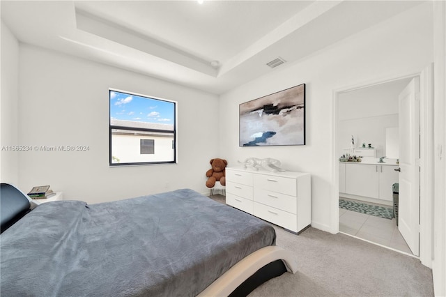 bedroom featuring light carpet, ensuite bath, and a raised ceiling