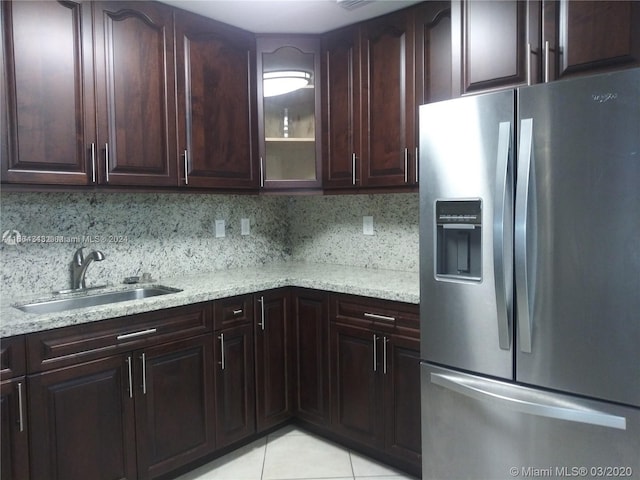 kitchen with light stone counters, stainless steel fridge, light tile patterned floors, sink, and tasteful backsplash