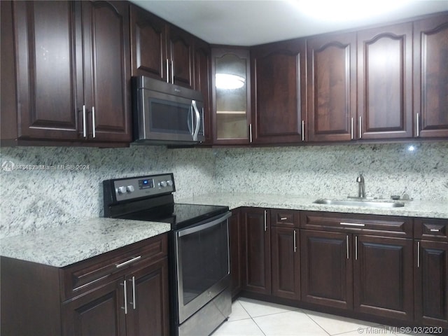 kitchen featuring appliances with stainless steel finishes, light tile patterned flooring, light stone counters, tasteful backsplash, and sink