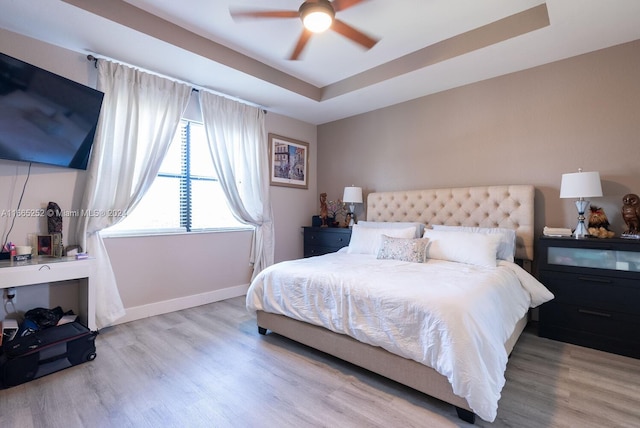 bedroom featuring a raised ceiling, ceiling fan, and light hardwood / wood-style flooring