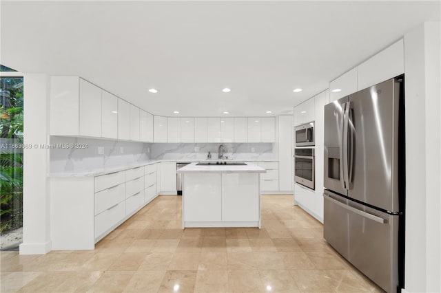 kitchen with decorative backsplash, white cabinetry, a kitchen island, stainless steel appliances, and sink