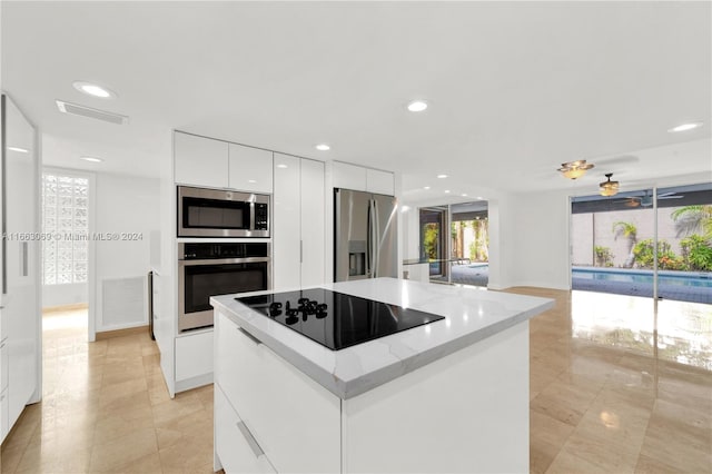 kitchen with ceiling fan, white cabinets, light stone counters, a kitchen island, and appliances with stainless steel finishes