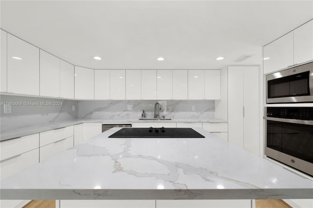 kitchen featuring sink, white cabinetry, stainless steel appliances, backsplash, and light stone countertops