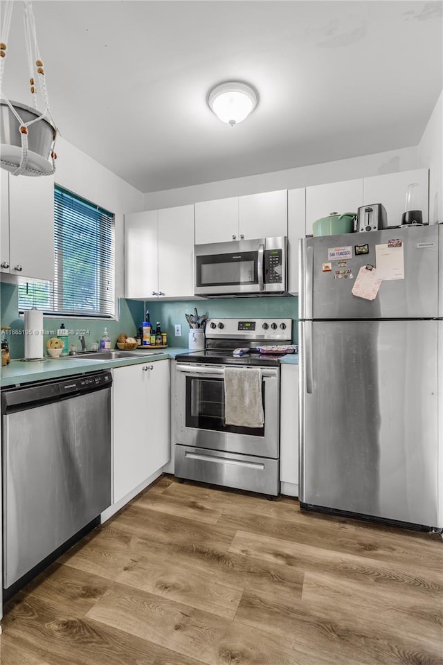 kitchen featuring wood-type flooring, stainless steel appliances, sink, and white cabinetry