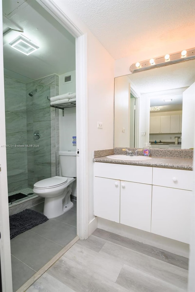 bathroom featuring vanity, tiled shower, a textured ceiling, and toilet