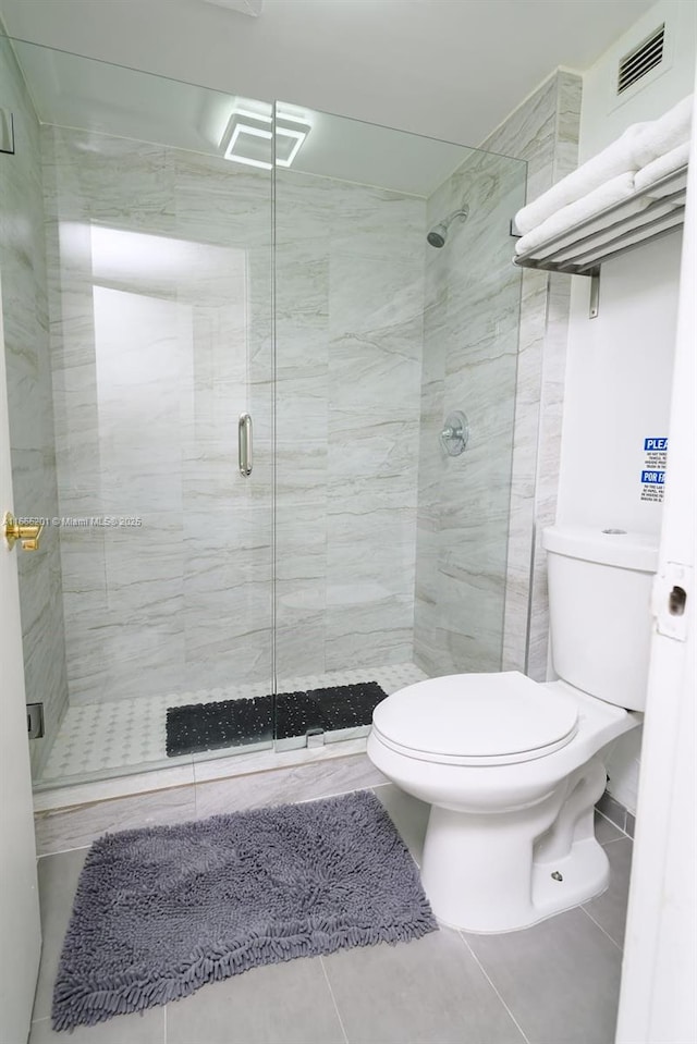 bathroom featuring tile patterned floors, toilet, and a shower with door