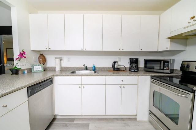 kitchen with stainless steel appliances, sink, white cabinets, and light hardwood / wood-style flooring