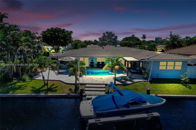 back house at dusk with a patio, a water view, and a yard