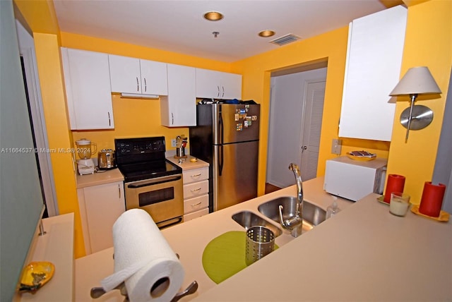 kitchen with electric range oven, stainless steel refrigerator, white cabinetry, and sink