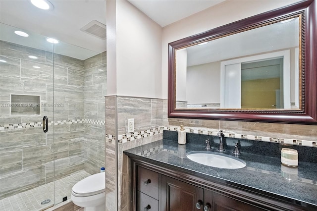 bathroom with vanity, tile walls, toilet, and a shower with door