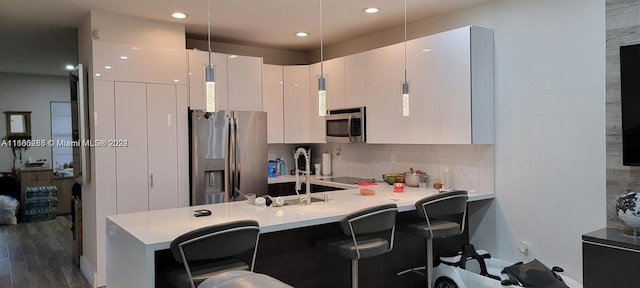 kitchen featuring appliances with stainless steel finishes, hanging light fixtures, white cabinets, kitchen peninsula, and dark hardwood / wood-style floors