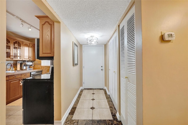 hallway with light tile patterned floors, a sink, a textured ceiling, track lighting, and baseboards