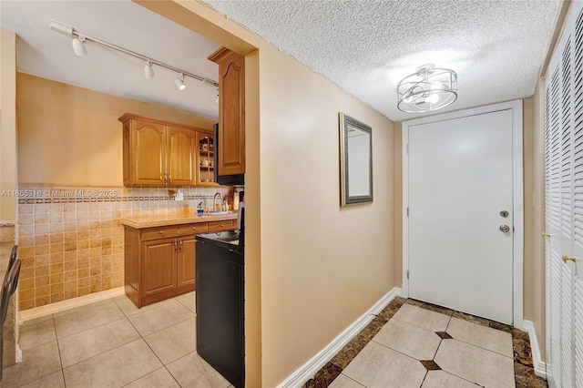 kitchen with light tile patterned floors, baseboards, black electric range oven, a textured ceiling, and tile walls