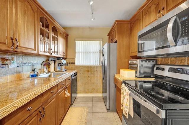 kitchen featuring appliances with stainless steel finishes, brown cabinetry, a sink, and light tile patterned floors