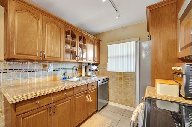 kitchen featuring brown cabinets, light tile patterned floors, stainless steel appliances, glass insert cabinets, and a sink