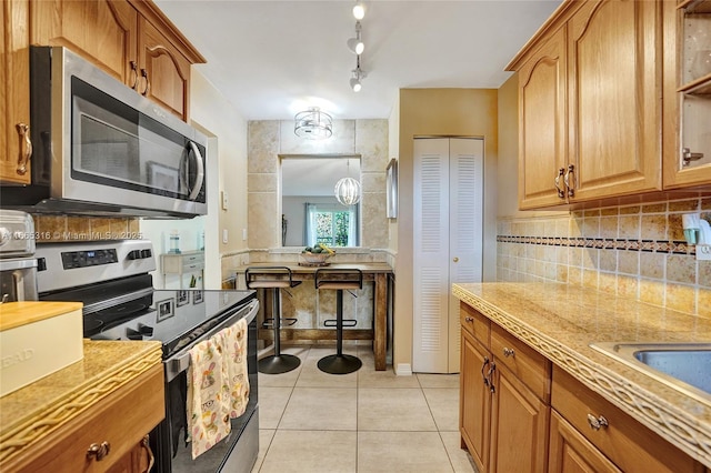 kitchen featuring light tile patterned floors, stainless steel appliances, light countertops, backsplash, and brown cabinets