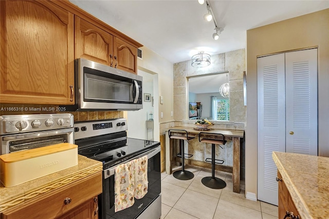 kitchen featuring light tile patterned floors, light countertops, appliances with stainless steel finishes, and brown cabinets