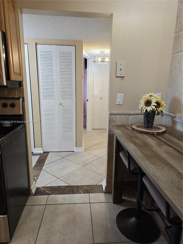 kitchen with light tile patterned flooring, black range with electric stovetop, and a textured ceiling