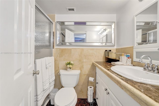 bathroom with visible vents, toilet, an enclosed shower, vanity, and tile walls