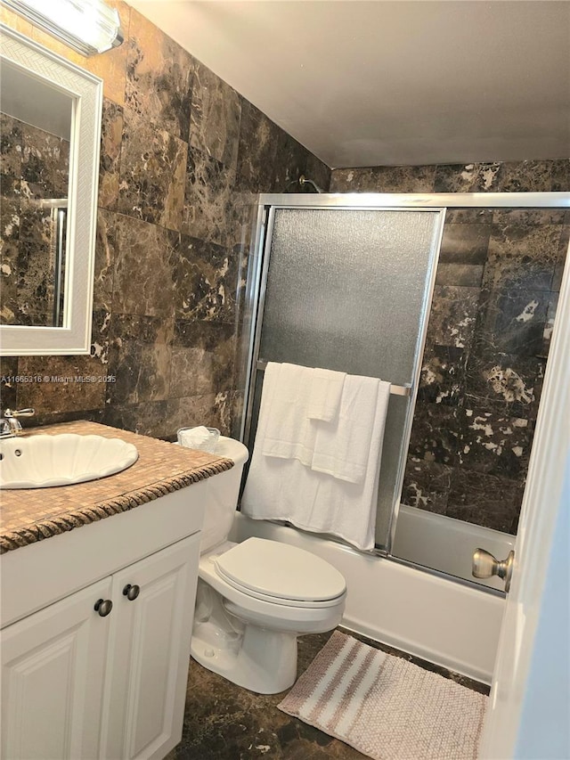 full bathroom with vanity, toilet, shower / bath combination with glass door, and tile walls