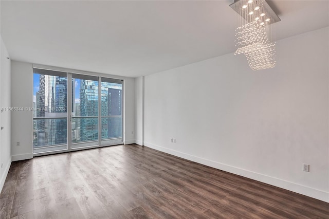 spare room with a notable chandelier, hardwood / wood-style flooring, a wall of windows, and plenty of natural light