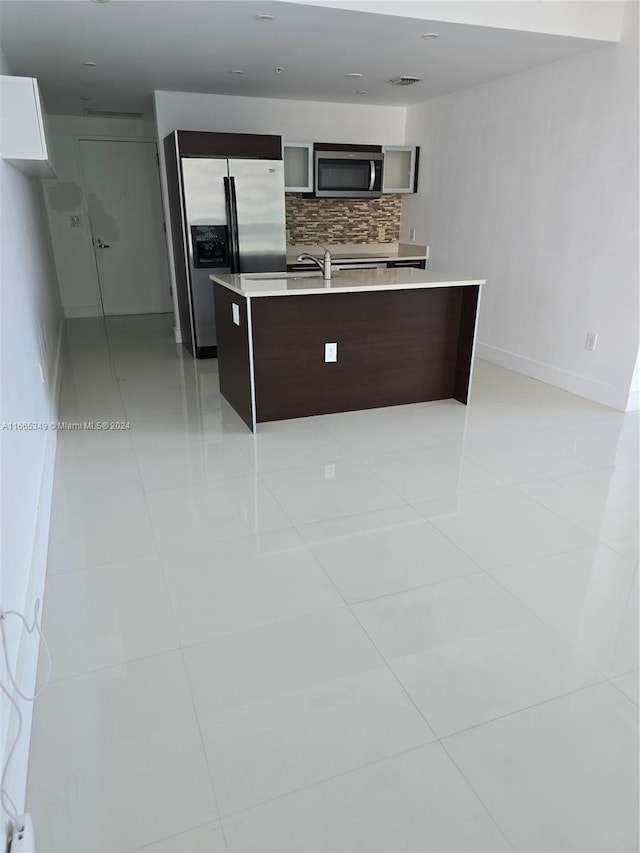 kitchen with a center island with sink, light tile patterned floors, stainless steel appliances, and tasteful backsplash