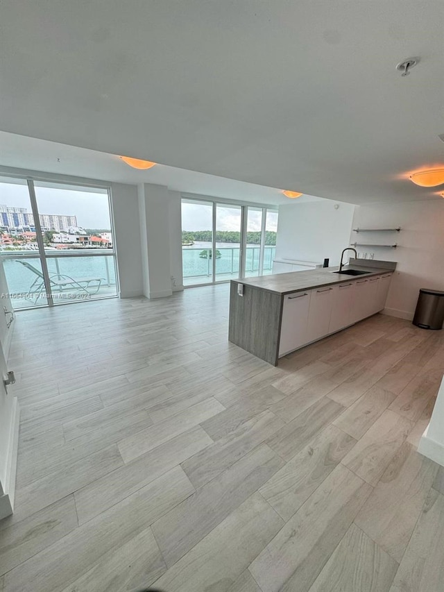 interior space with a kitchen island with sink, light wood-type flooring, sink, and white cabinetry