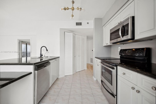 kitchen featuring appliances with stainless steel finishes, white cabinets, light tile patterned floors, sink, and a chandelier