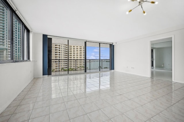 tiled spare room with expansive windows and a chandelier