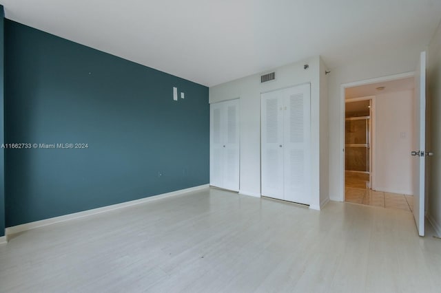 unfurnished bedroom featuring light hardwood / wood-style flooring and multiple closets