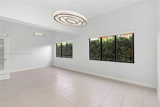 tiled spare room featuring an inviting chandelier