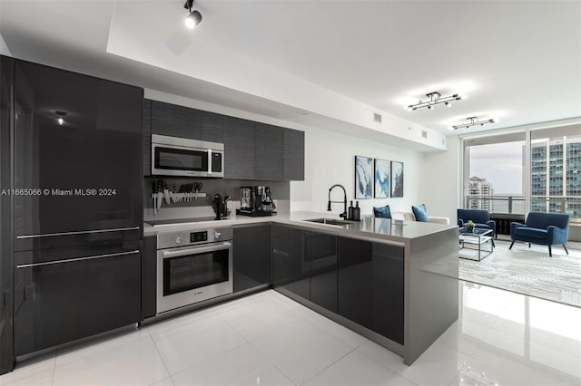 kitchen with light tile patterned floors, sink, kitchen peninsula, rail lighting, and appliances with stainless steel finishes