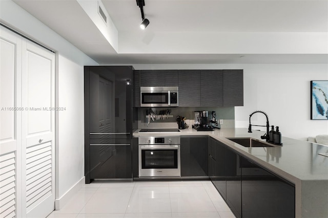 kitchen featuring rail lighting, kitchen peninsula, light tile patterned floors, stainless steel appliances, and sink